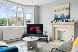 Un salon doté d’une cheminée, d’un téléviseur diffusant du contenu « NETFLIX », et offrant une vue sur l’extérieur grâce à de grandes fenêtres.