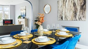 Ein Essbereich mit einem schwarzen Tisch, goldenen Platzsets, weißen Tellern und blauen Stühlen.