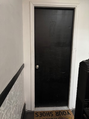 Una puerta negra con pomo, un zócalo blanco y un felpudo con texto.