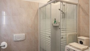 A modern bathroom with a glass-enclosed shower, a toilet paper holder, and a washing machine. - Stylish boutique apartment with Elbe view & hotel comfort (Meißen)