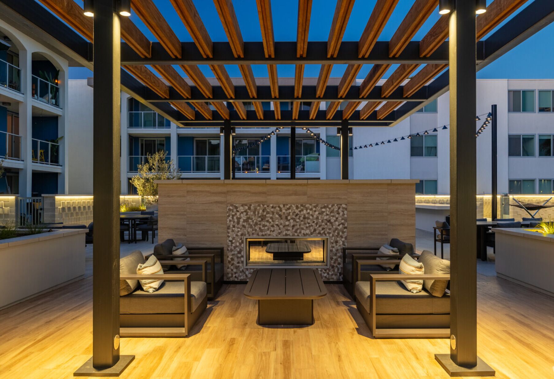 Un espace extérieur aménagé en terrasse, doté d’un foyer intégré, de coins salon et d’une structure en forme de pergola.