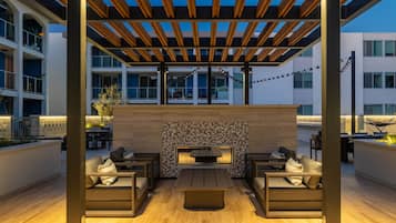 An outdoor patio area with a built-in fireplace, seating arrangements, and a pergola structure.