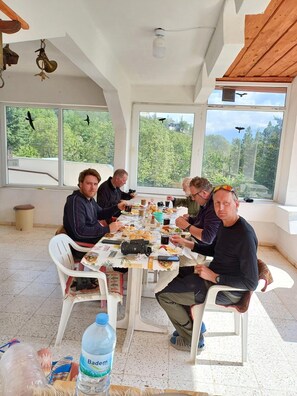 Un grupo de personas cenando en una mesa con vistas a árboles y aves silvestres.