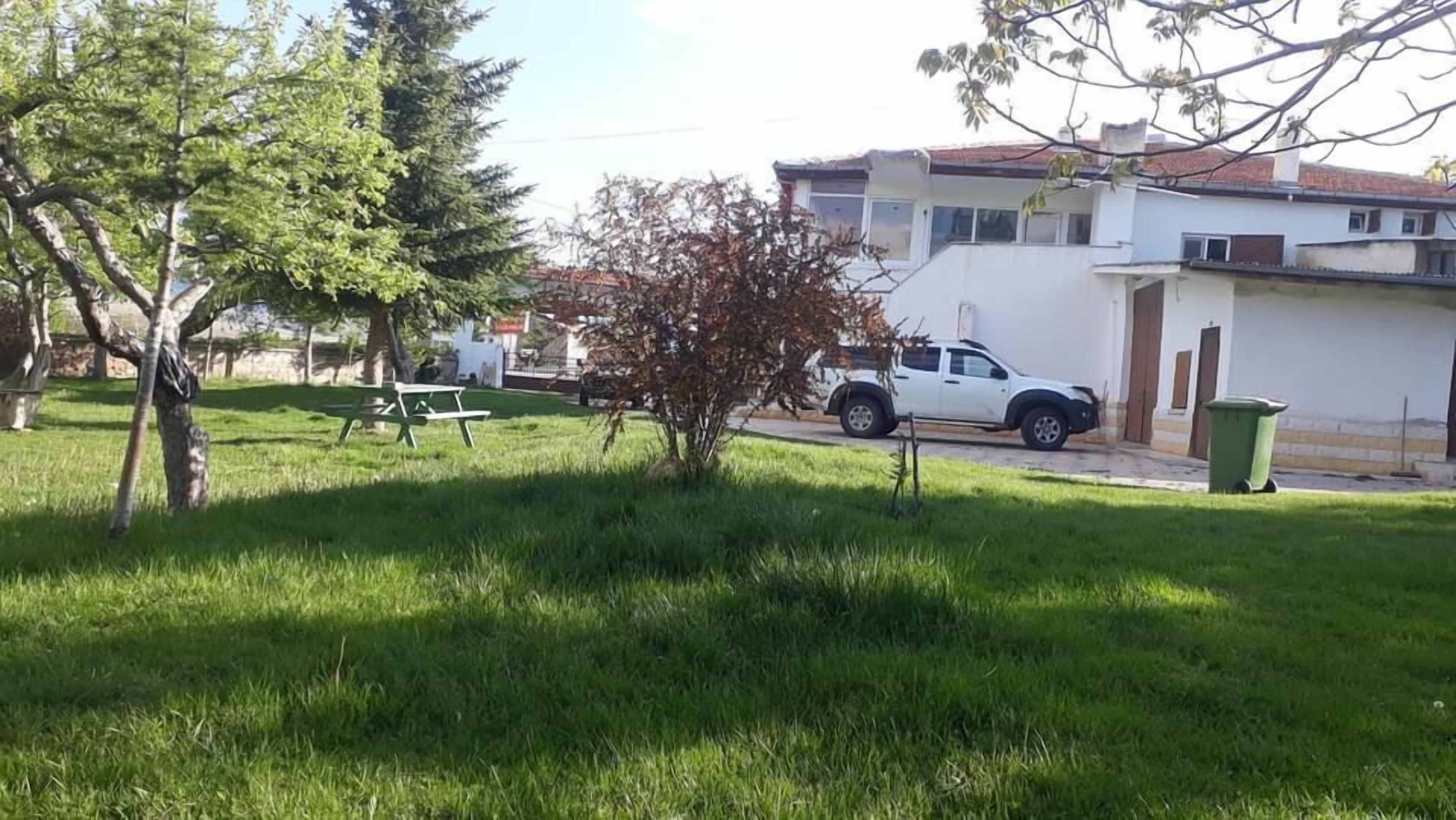 A grassy area with a picnic table, a white vehicle, and a building in the background.