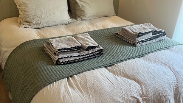 A neatly made bed with a green quilt, white linens, and folded towels. - Le Clos des Berges de l'Ain - House 8/10 pers with swimming pool on the river bank - France (Charnoz-sur-Ain)