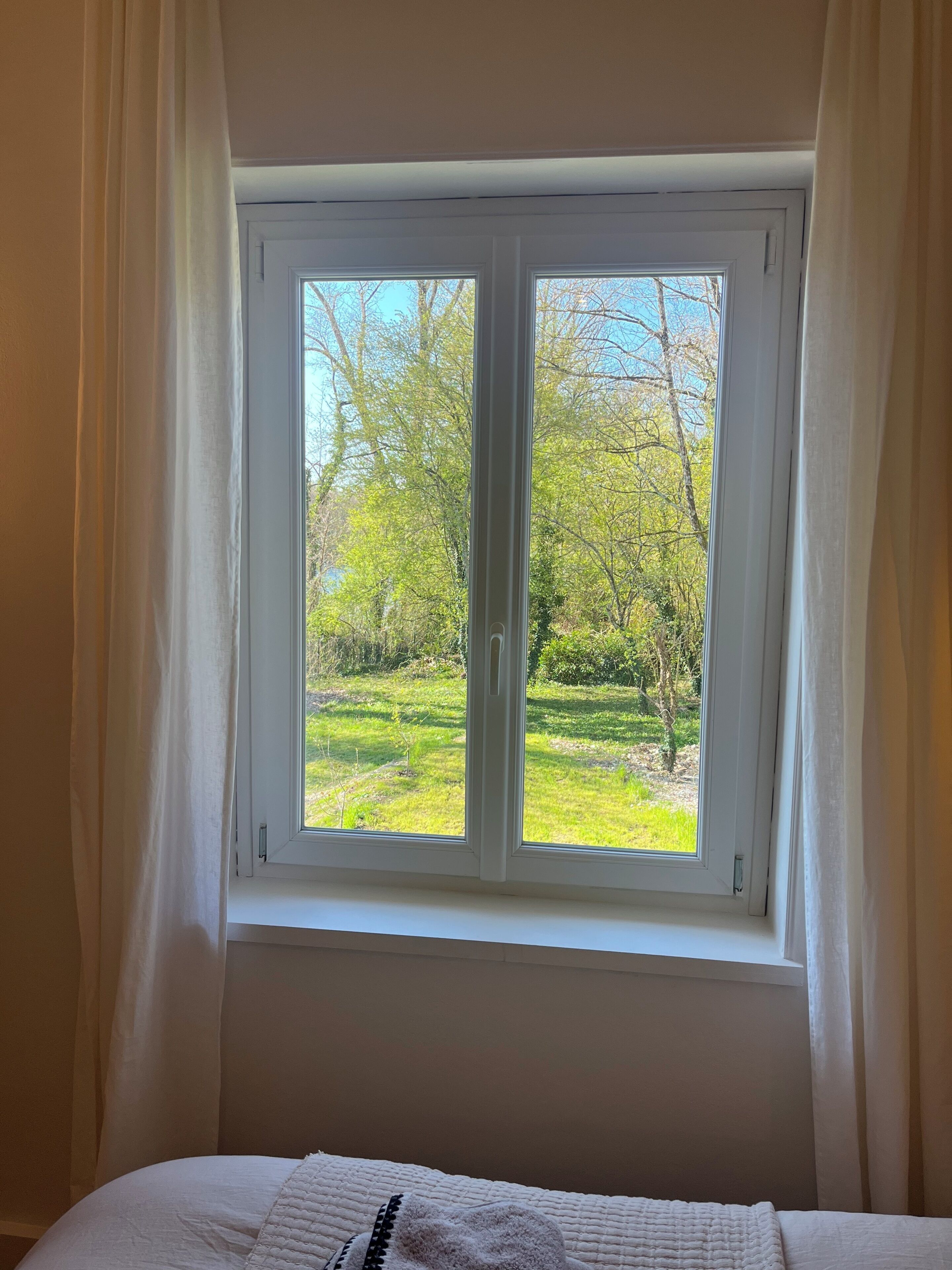 A bedroom with a large window, a bed, and a view of a green park.