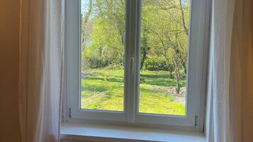 A bedroom with a large window, a bed, and a view of a green park.