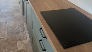 A modern kitchen with a wooden countertop, a black cutting board, a built-in oven, and a wall-mounted air conditioner. - Le Clos des Berges de l'Ain - House 8/10 pers with swimming pool on the river bank - France (Charnoz-sur-Ain)