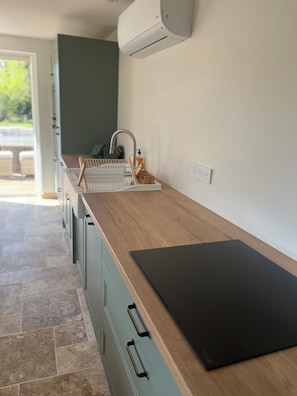 A modern kitchen with a wooden countertop, a black cutting board, a built-in oven, and a wall-mounted air conditioner. - Le Clos des Berges de l'Ain - House 8/10 pers with swimming pool on the river bank - France (Charnoz-sur-Ain)