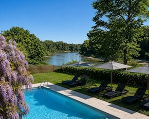 A swimming pool with lounge chairs and umbrellas, surrounded by greenery and a river view. - Le Clos des Berges de l'Ain - House 8/10 pers with swimming pool on the river bank - France (Charnoz-sur-Ain)