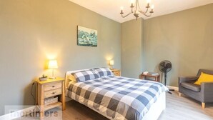 Een slaapkamer met een groot bed, nachtlampen, een ventilator, een grijze bank en een stadsgezichtschilderij aan de muur.