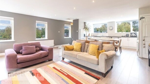 Een moderne woonkamer met twee banken, een keukenhoek en grote ramen.