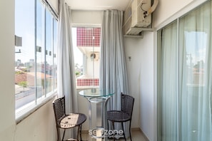 Ein Balkon mit Glastisch und zwei Korbstühlen, eine Schiebetür und eine Klimaanlage.