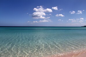 Ein klares türkisfarbenes Meer, ein Sandstrand und ein entfernter Segelboot.