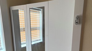 Un armario blanco con dos puertas y una ventana, situado en una habitación con suelo de madera y paredes beige.