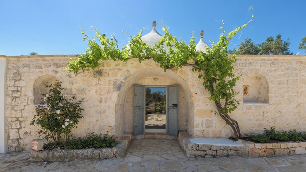 An entrance with a stone archway, a vine-covered wall, and a clear blue sky. - Trullo Cecapesce by Perle di Puglia (Carovigno)
