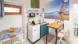 Een compacte keuken met een koelkast, magnetron, spoelbak en een eettafel met stoelen.