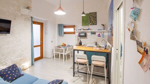 Een ruimtelijk ingerichte leefruimte met eethoek, kitchenette en een aan de muur bevestigde televisie.