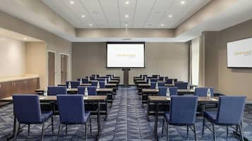Un salón de conferencias con una pantalla grande que muestra 'COURTYARD' y una presentación, con mesas y sillas dispuestas.