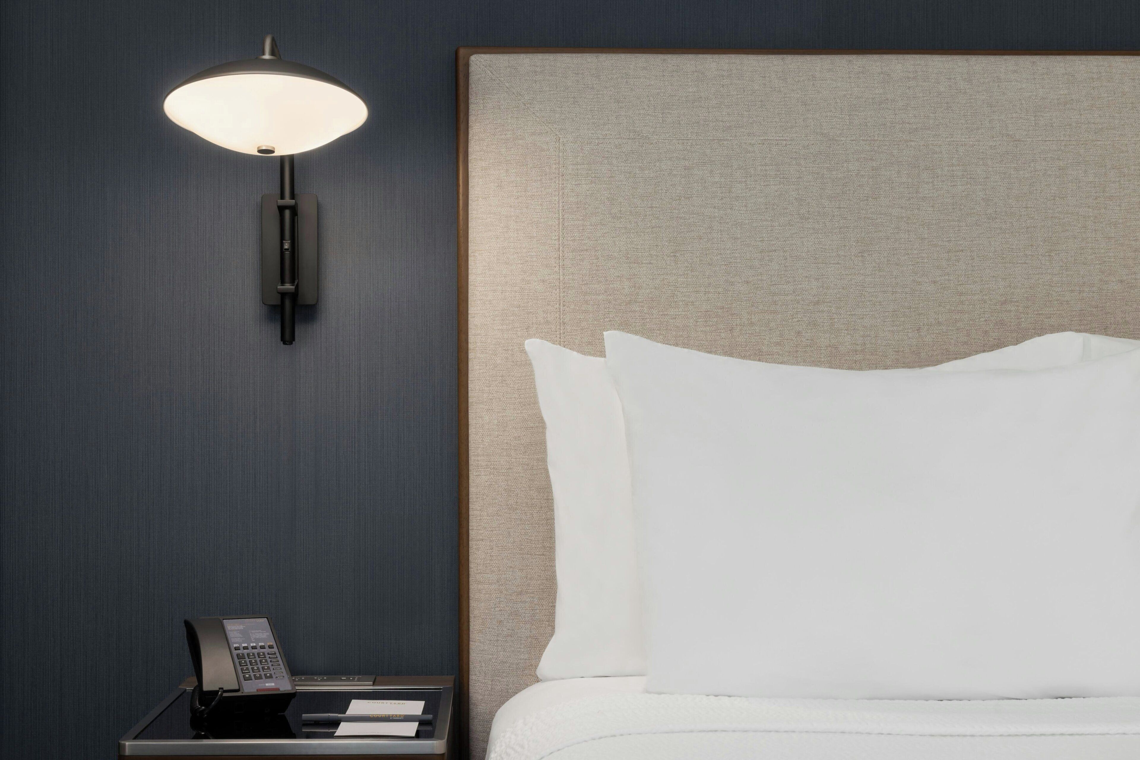 A hotel room with a bed, a nightstand, a lamp, and a telephone.