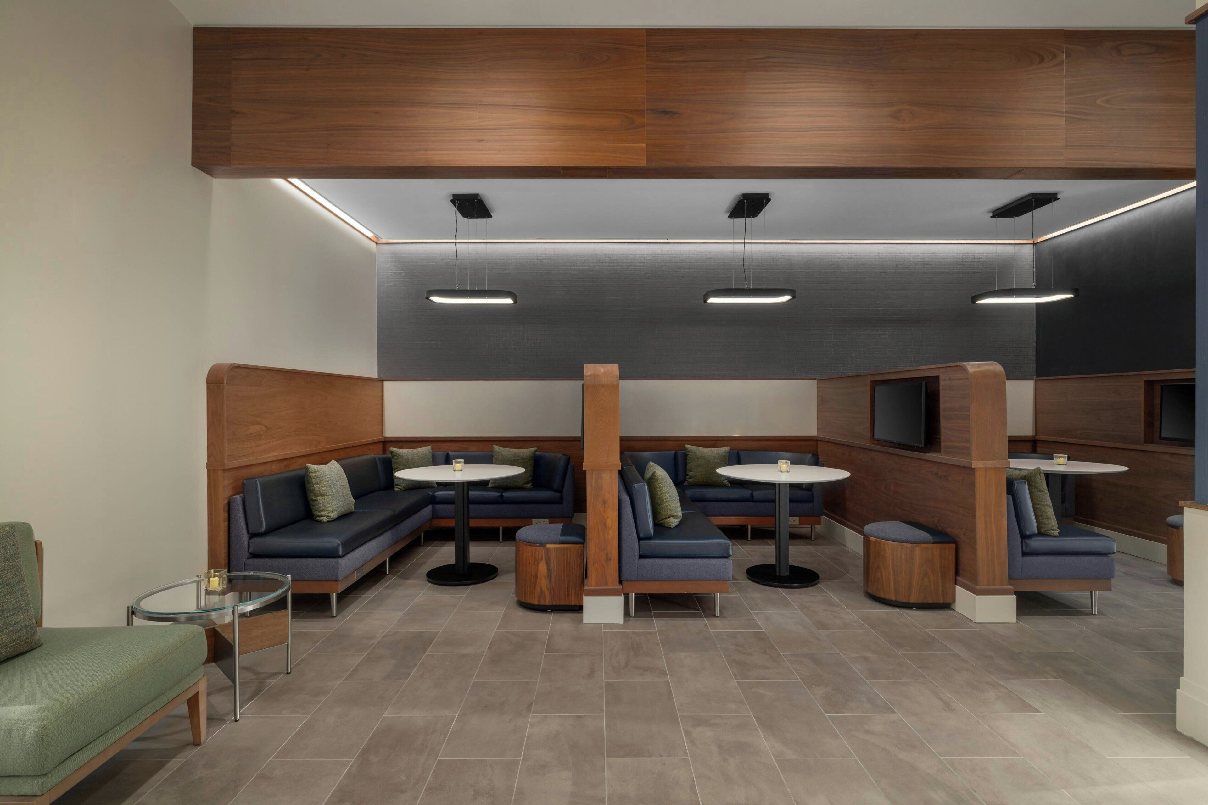A modern lounge area with sofas, round tables, and a TV screen.