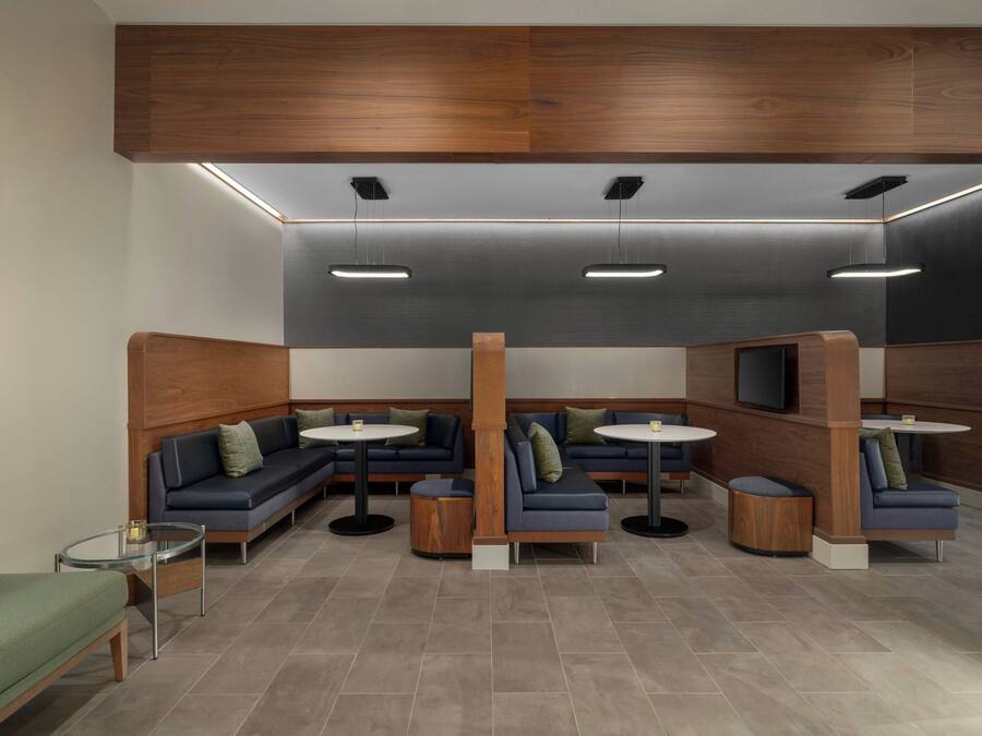 A modern lounge area with sofas, round tables, and a TV screen.