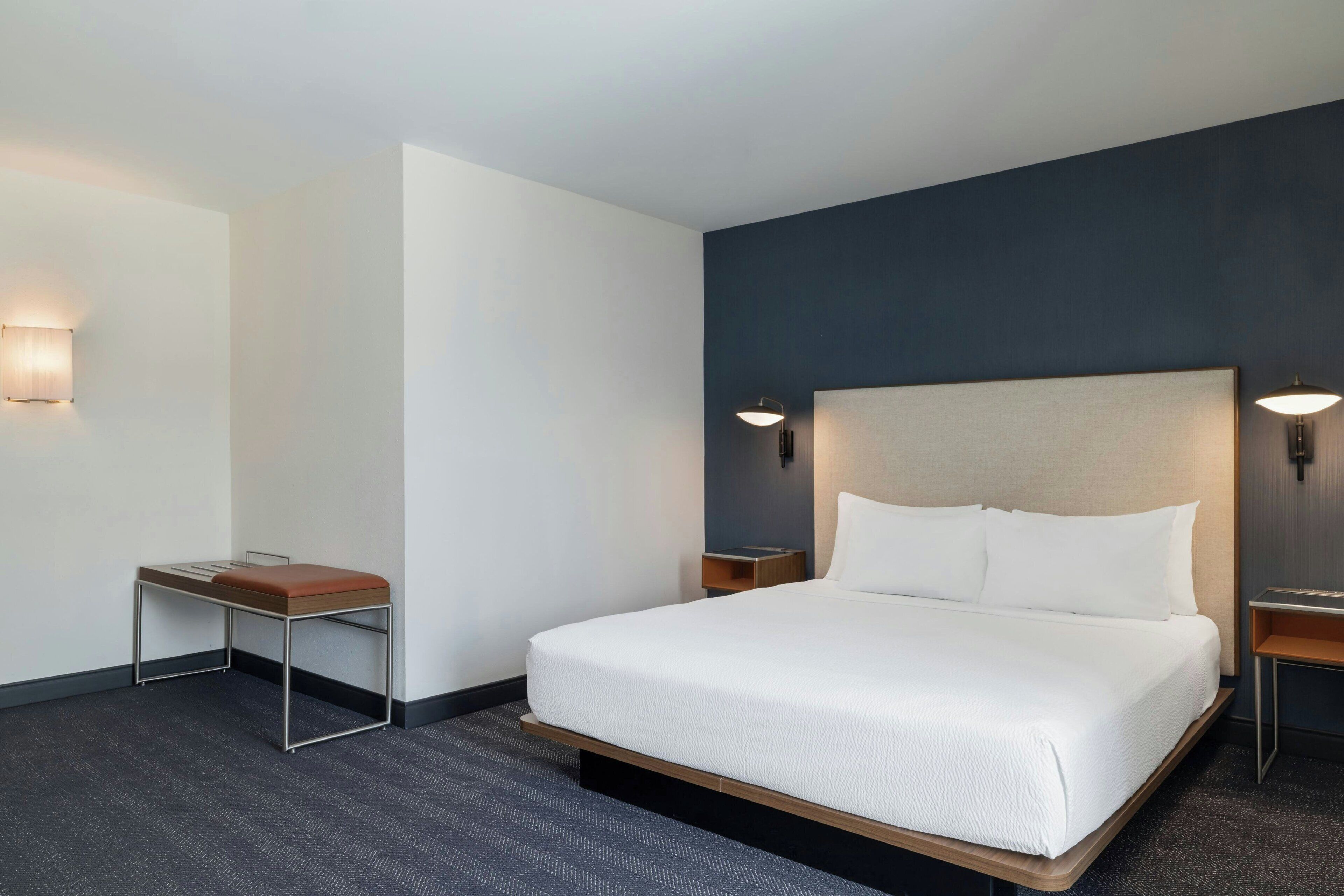 A hotel room with a single bed, a small table, two bedside tables, and wall-mounted lamps.