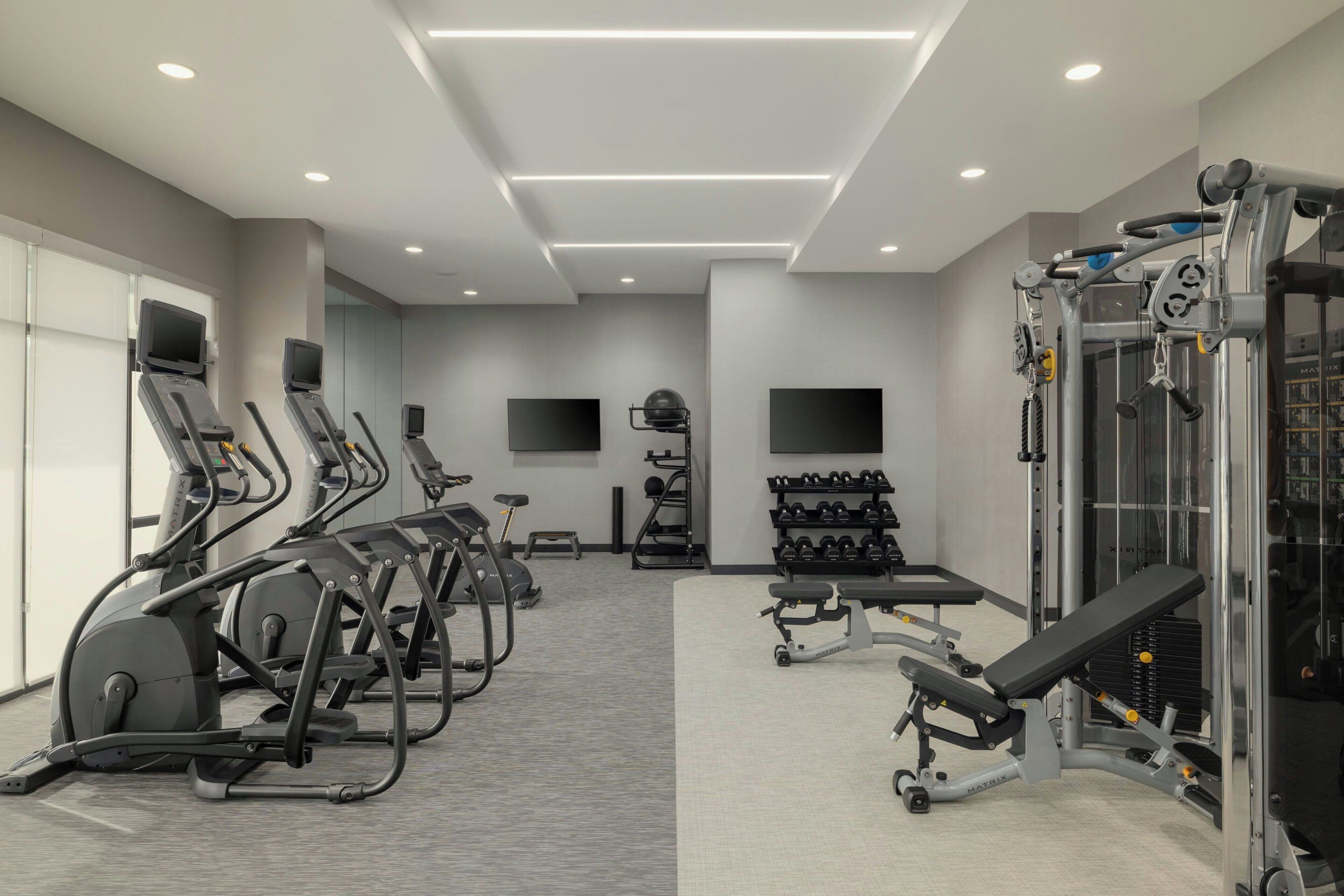 Une salle de sport équipée de tapis de course, d’appareils de musculation et d’haltères.