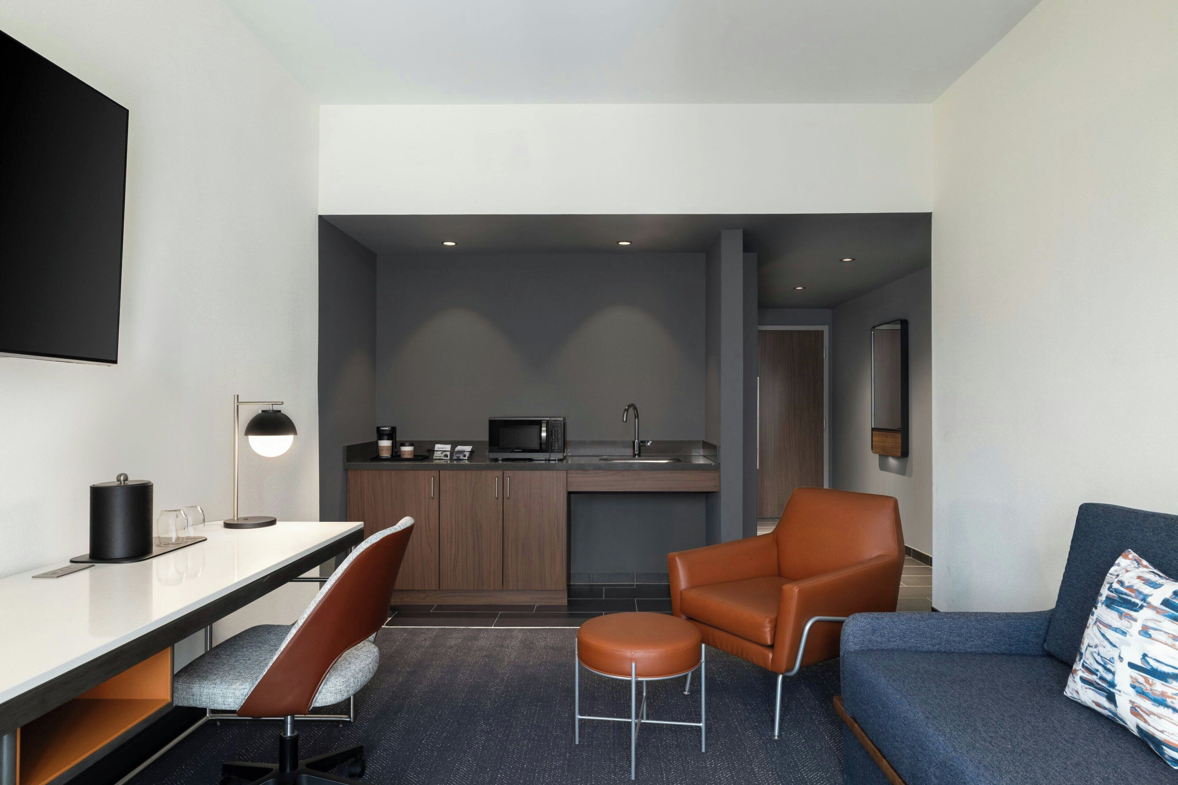Una habitación de hotel moderna con kitchenette, un sofá, una mesa de comedor con sillas y un televisor montado en la pared.