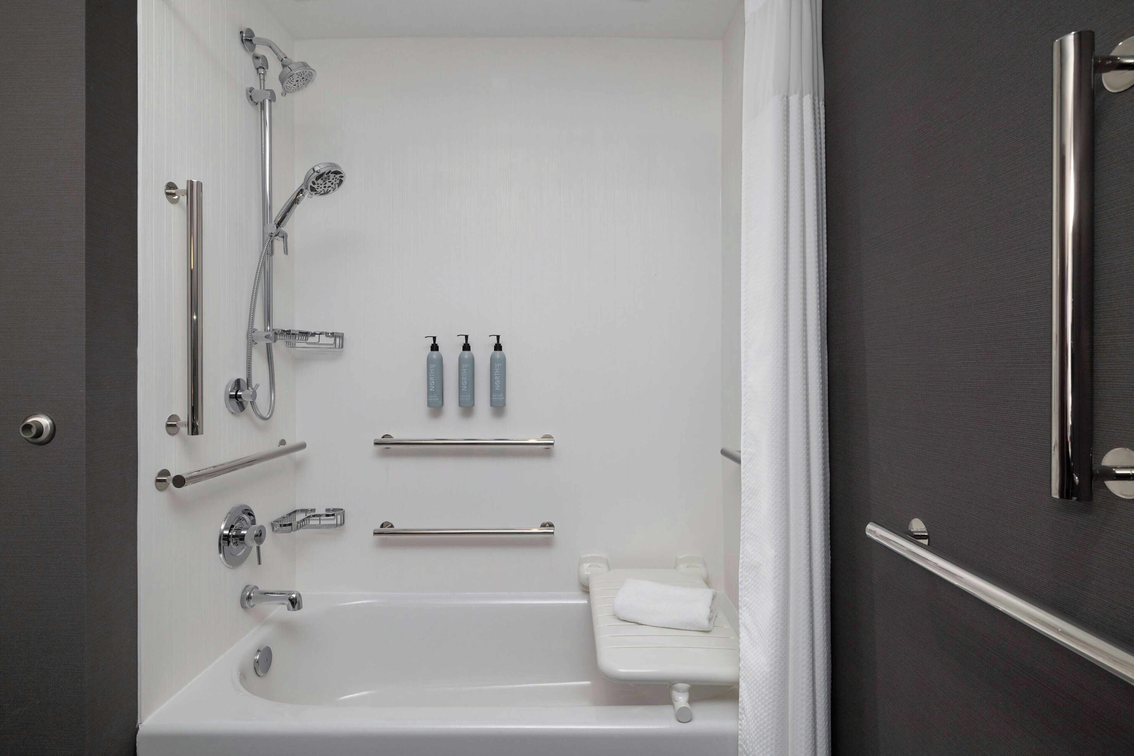 Un baño moderno con bañera, ducha, barras de apoyo y un inodoro.