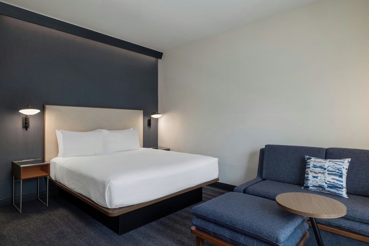 Et hotelværelse med en seng, en sofa, et lille bord og to væglamper.