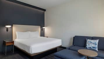 Habitación de hotel con cama, sofá, una mesita y dos lámparas fijadas a la pared.