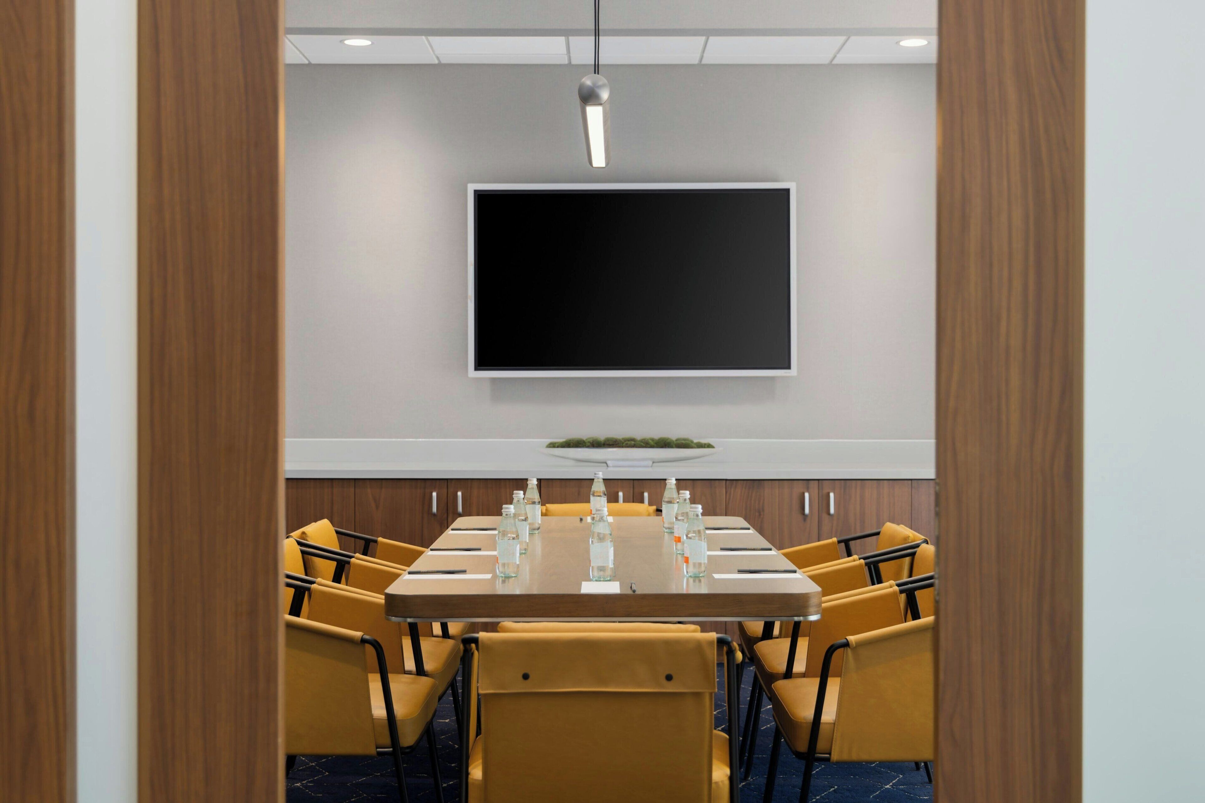 A conference room with a large table, yellow chairs, a flat-screen TV, and a wooden accent wall.