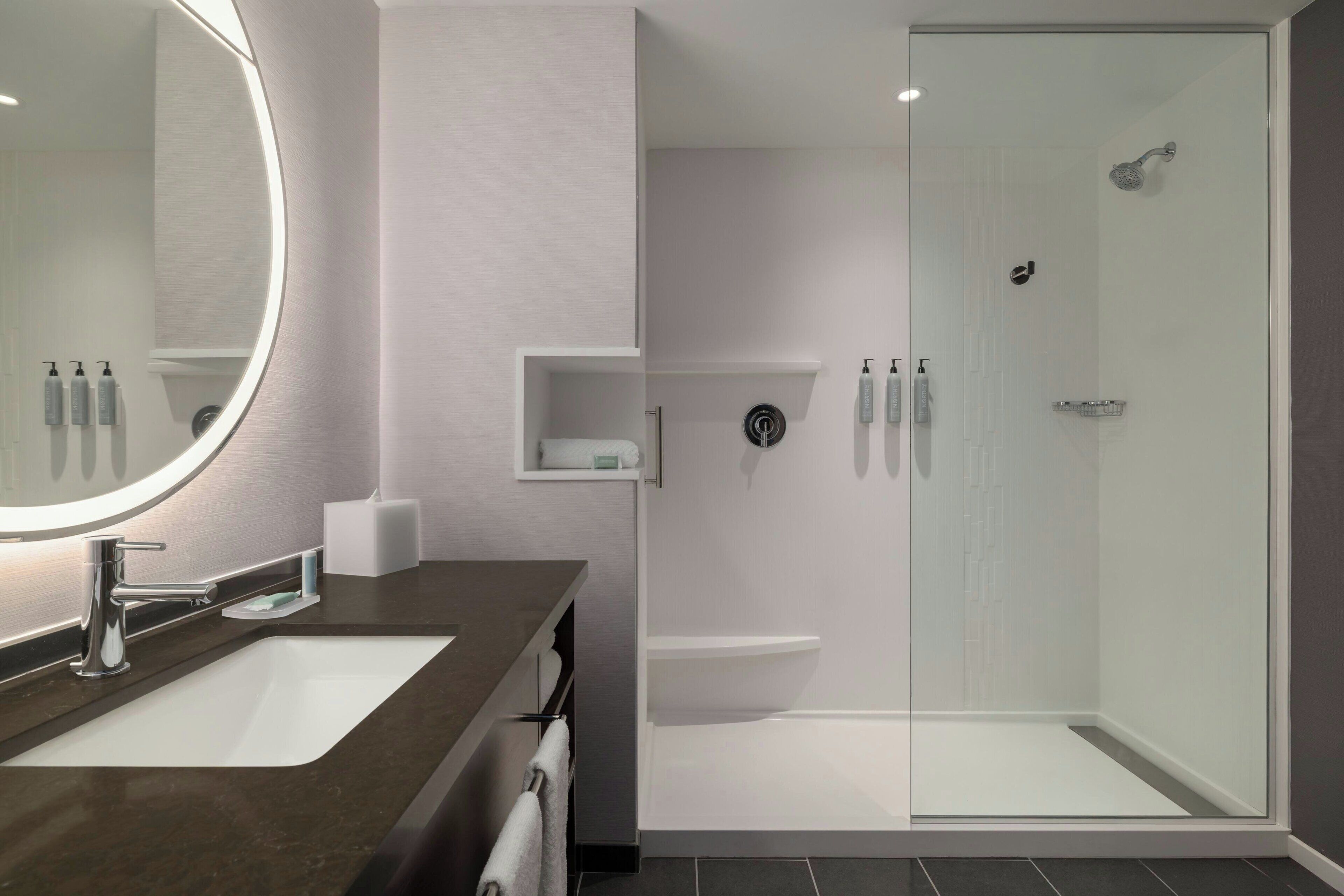 A modern bathroom with a large mirror, a sink, a toilet, and a glass-enclosed shower.