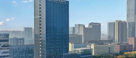 A modern high-rise hotel with a prominent 'Four Points' sign, surrounded by other buildings and a clear sky.