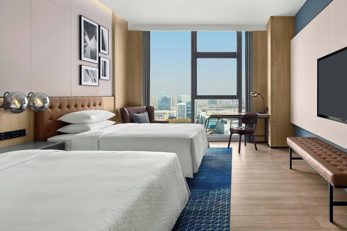A hotel room with two beds, a desk, a chair, and a large TV.