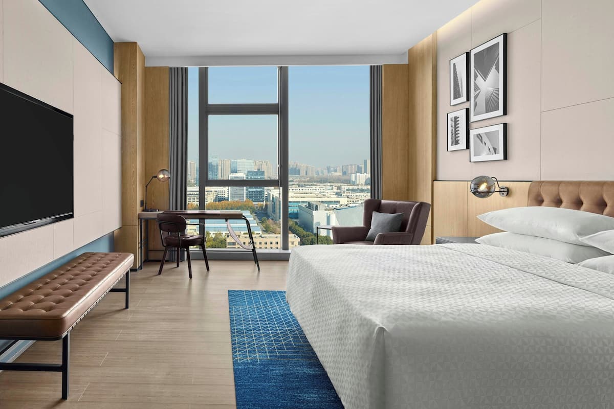 A hotel room with a large bed, a bench, a desk, and a TV.