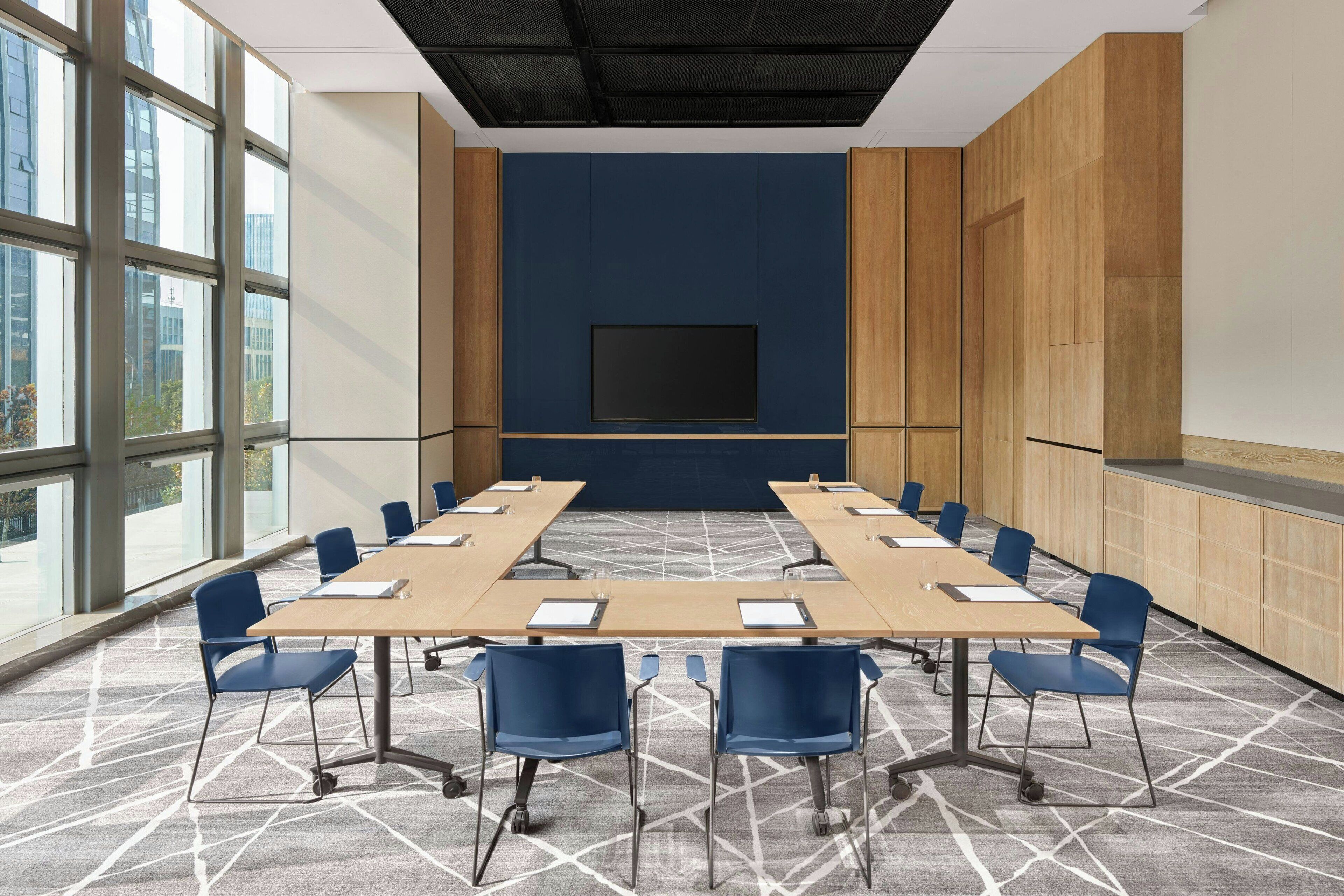 A conference room with a large table, blue chairs, a flat-screen TV, and large windows.