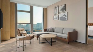 Une chambre d’hôtel moderne dotée d’une grande fenêtre donnant sur la ville, d’un canapé, d’une table basse ronde et d’un téléviseur.