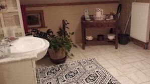 Une salle de bain avec un lavabo, des plantes en pot, un tapis à motifs, une petite table avec des articles de toilette et un espace douche.