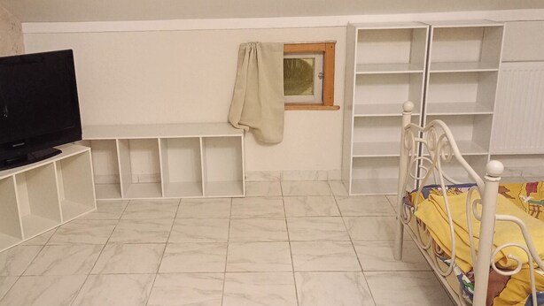 Une pièce avec un téléviseur posé sur un meuble, un lit recouvert d’une couvre-lit colorée et des étagères intégrées.