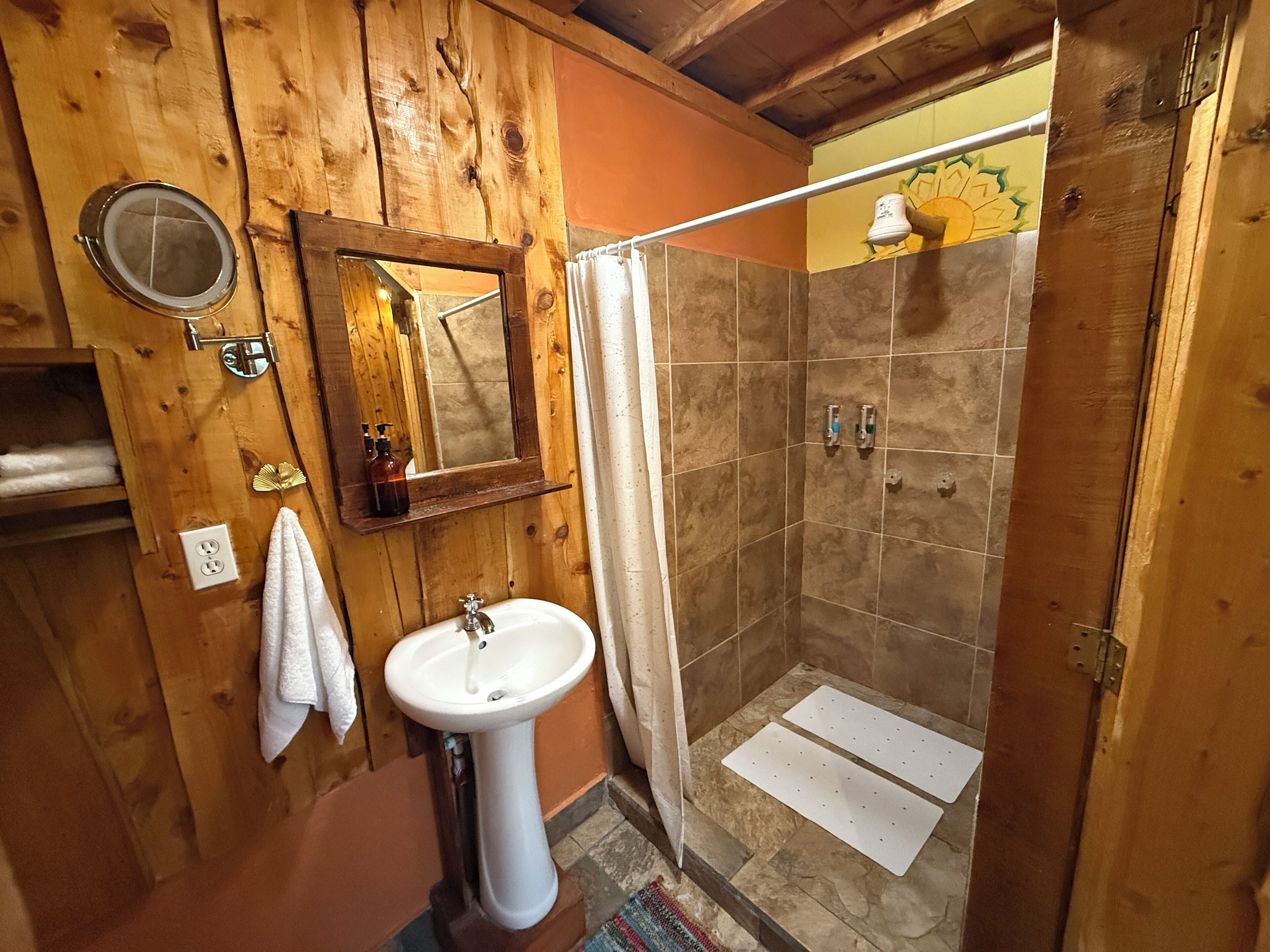 A wooden bathroom with a pedestal sink, a mirror, and a shower area.