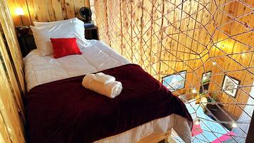 Una habitación tipo cabaña de madera con una cama, un cojín rojo, un cojín blanco, una manta roja y una toalla blanca sobre la cama.