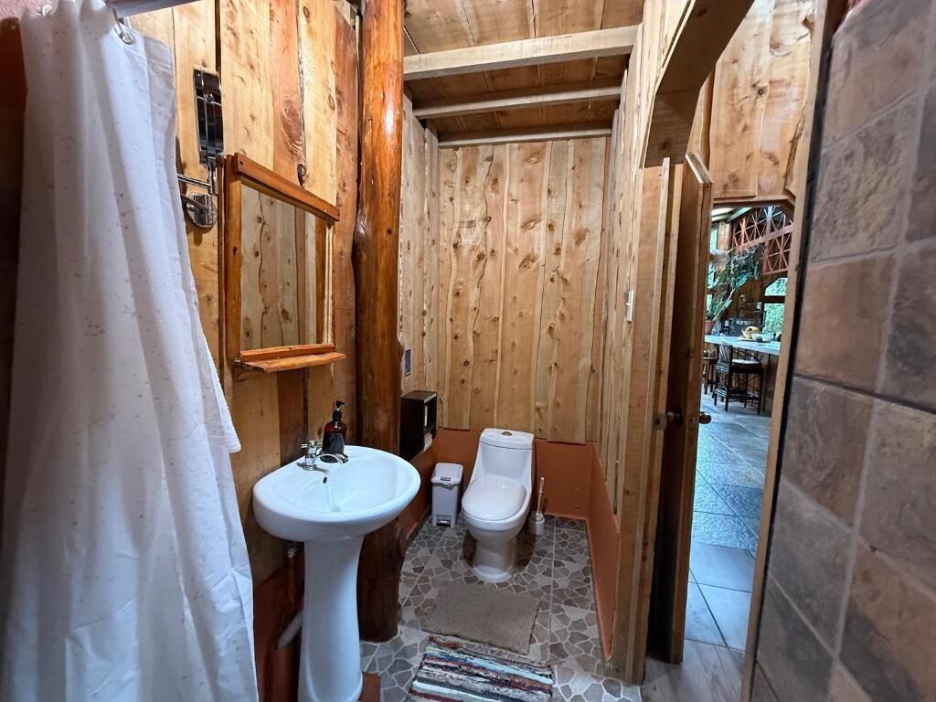 A small bathroom with wooden walls, a white sink, and a toilet.