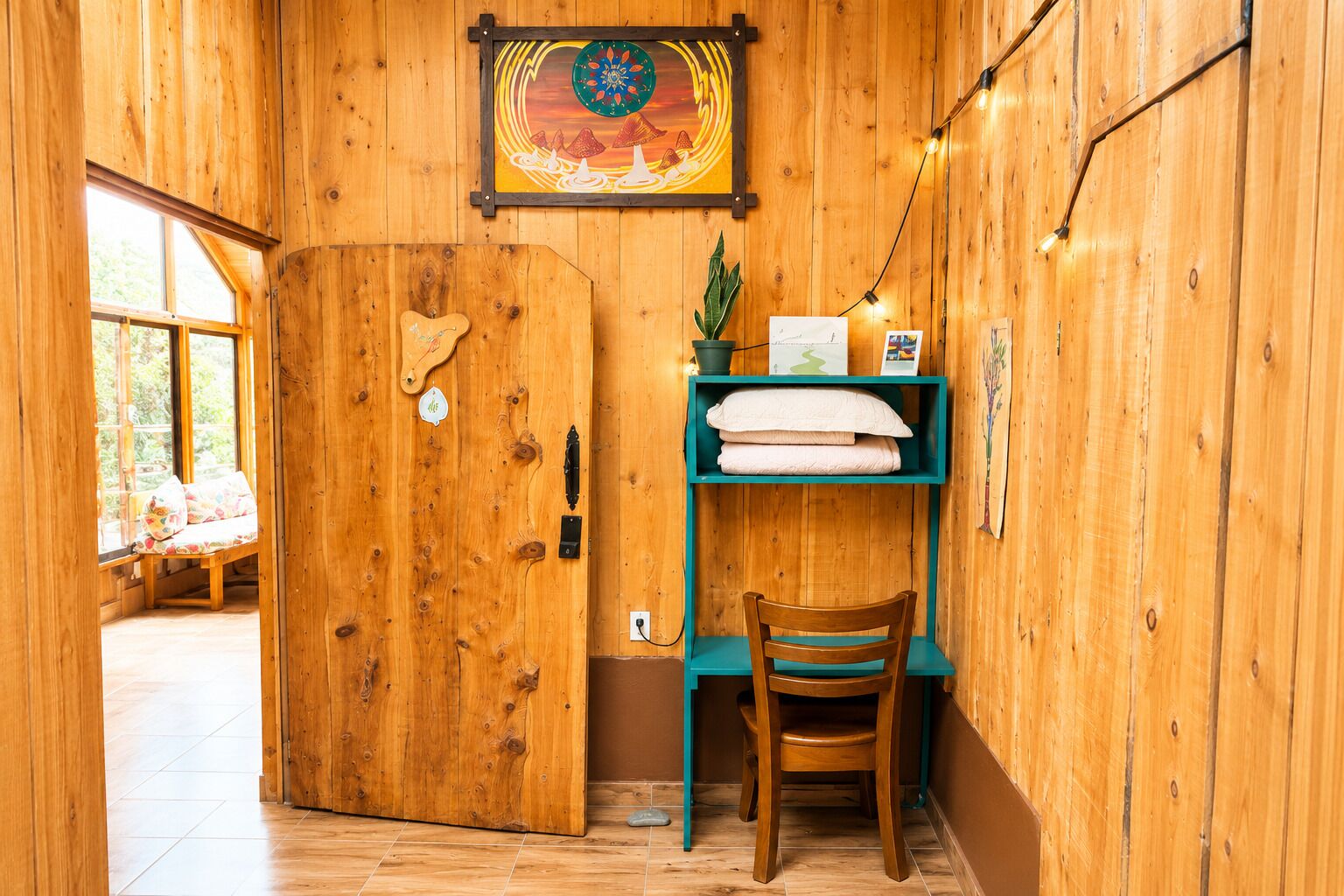 A wooden interior with a door, a shelf with towels, a chair, and a wall-mounted picture.