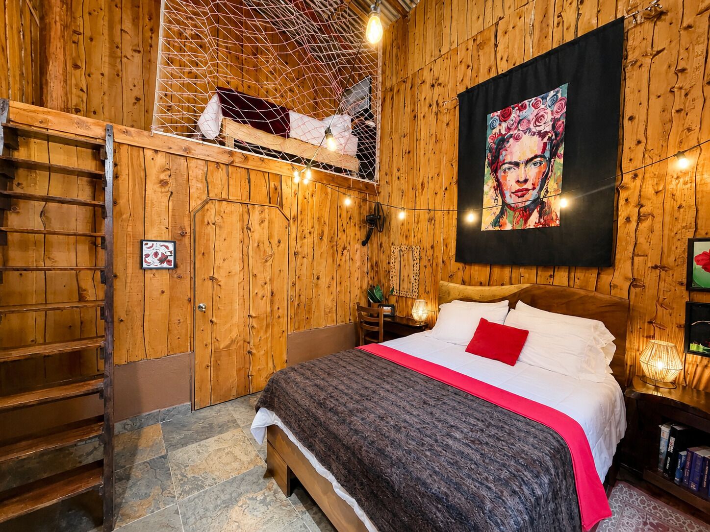 A wooden room with a bed, a ladder, and a painting on the wall.