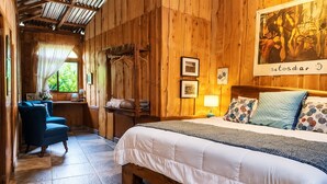 A wooden room with a bed, a chair, a desk, and a window.