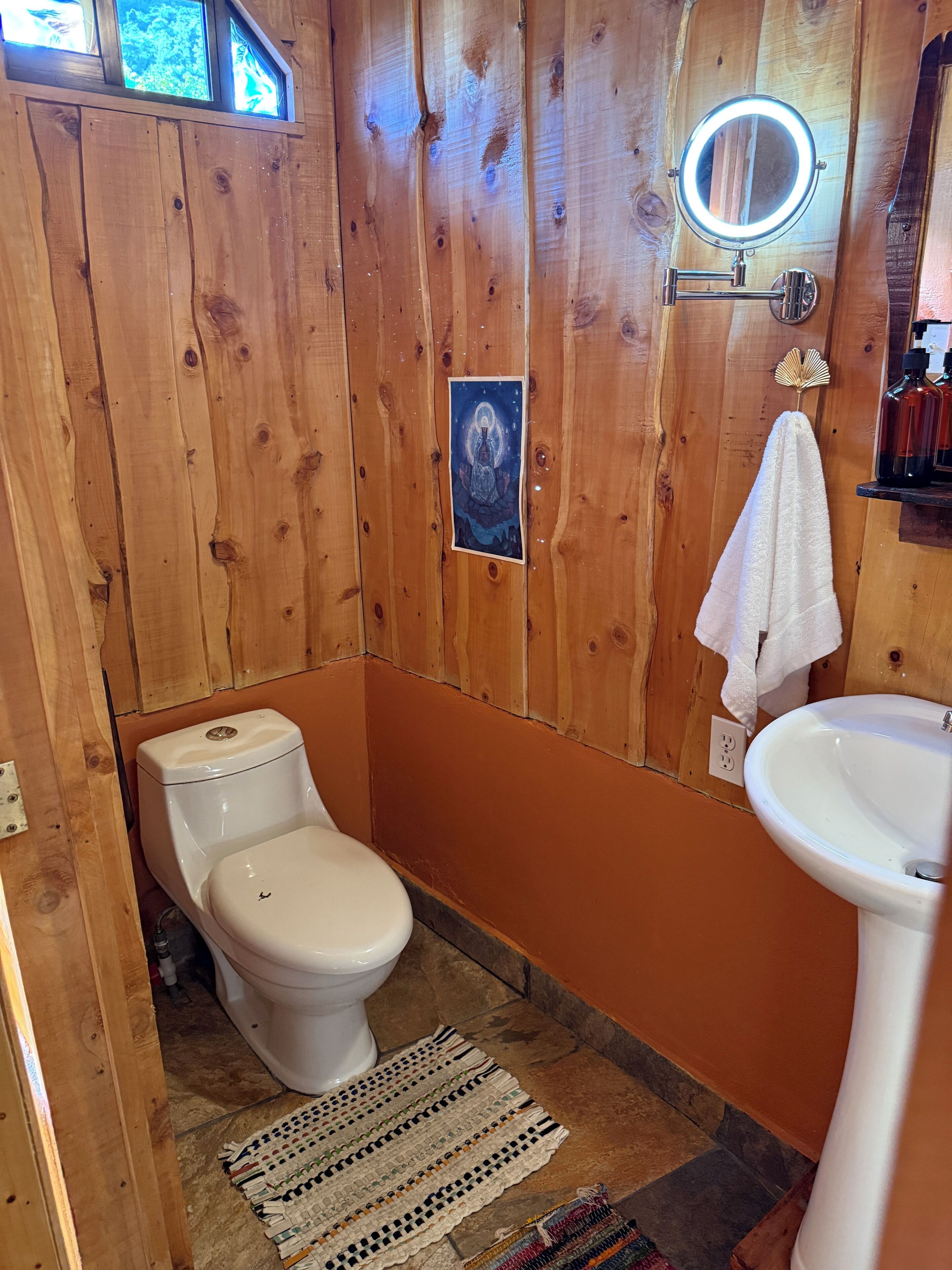 A wooden bathroom with a toilet, sink, and a small window.