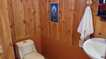 Ein Badezimmer aus Holz mit Toilette, Waschbecken und einem kleinen Fenster.