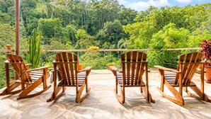 A terrace with wooden rocking chairs, a view of a lush forest, and a clear sky.